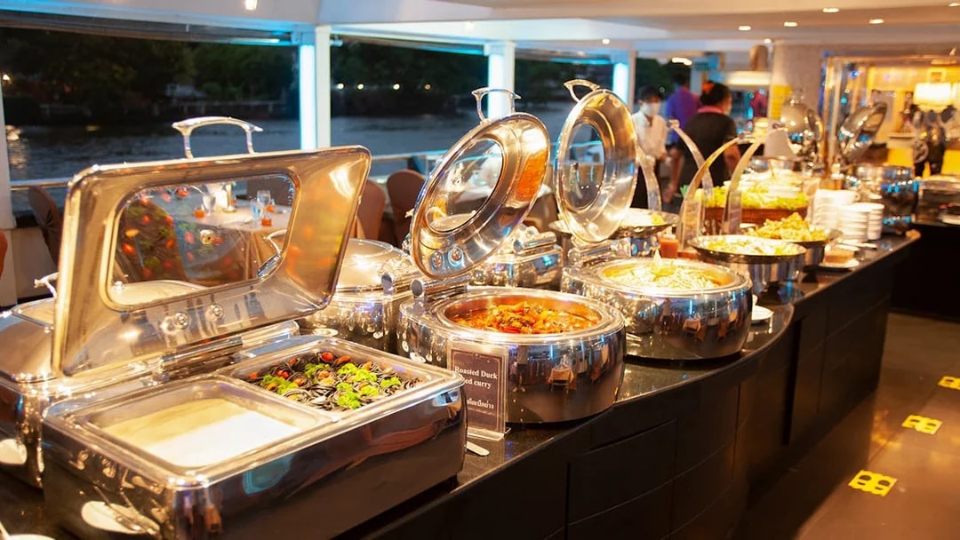 Buffet setup on Chao Phraya Cruise with various dishes and river view.