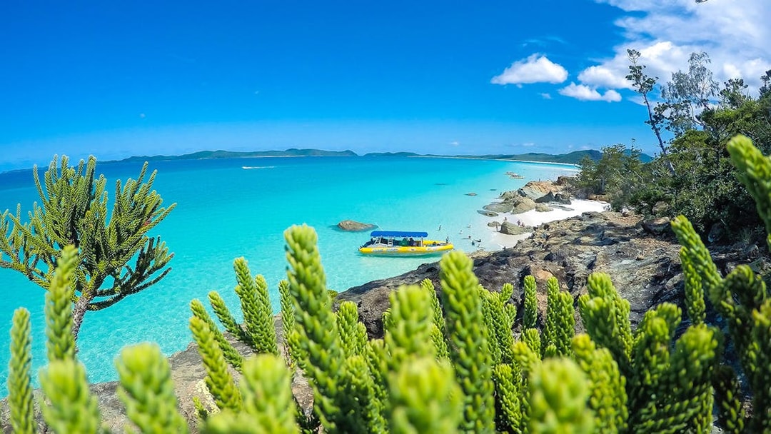 Whitsundays beach with turquoise water and a yellow raft near rocky shore.