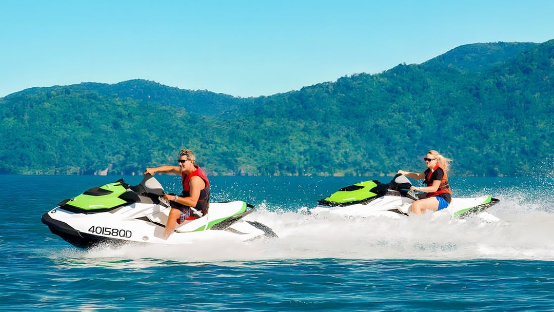 Tourists riding jetskis in the Whitsundays with lush green hills in the background.