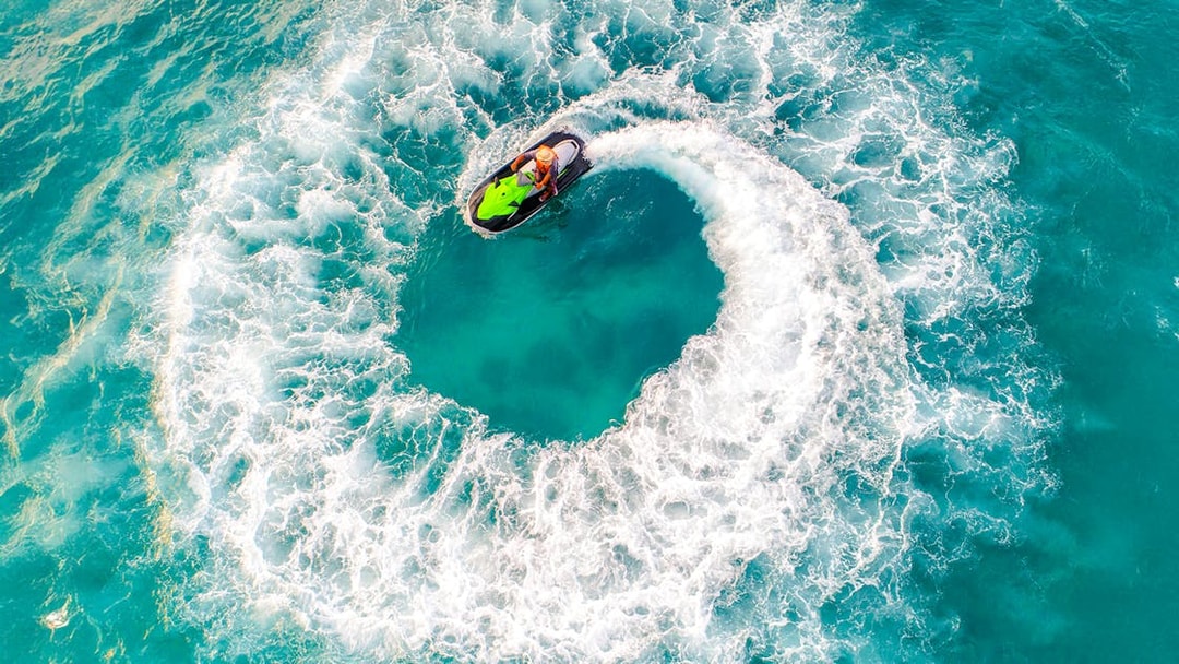 Aerial view of a person riding a jet ski in a circular motion on turquoise water.