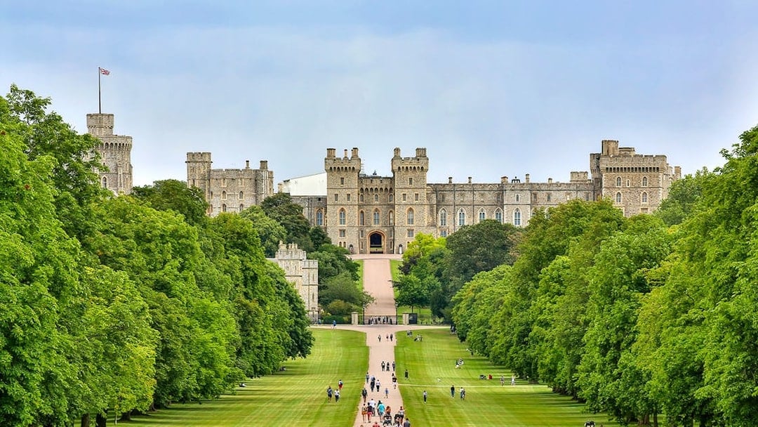 Tourists walking towards Windsor Castle through a tree-lined path on a day trip from London.