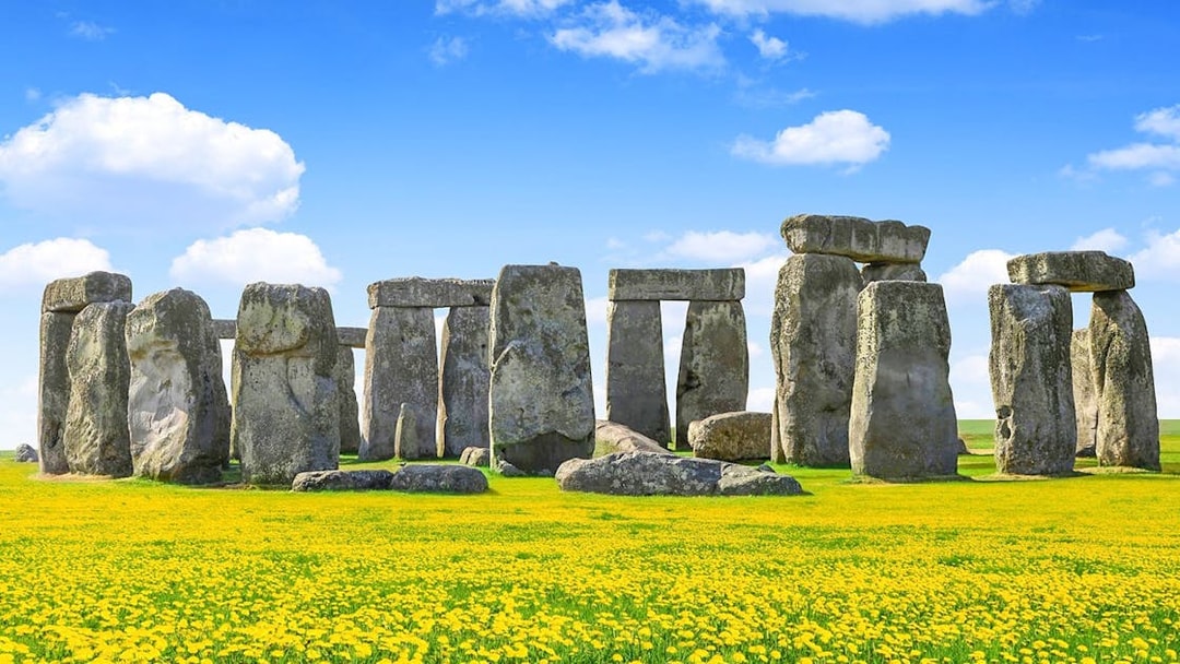 Stonehenge with blue sky and yellow flowers during daytime.