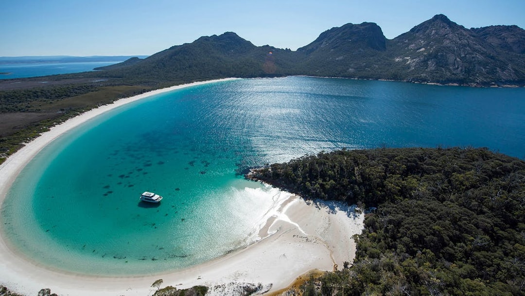 Cruise boat in Wineglass Bay, Tasmania, surrounded by turquoise water and lush hills.