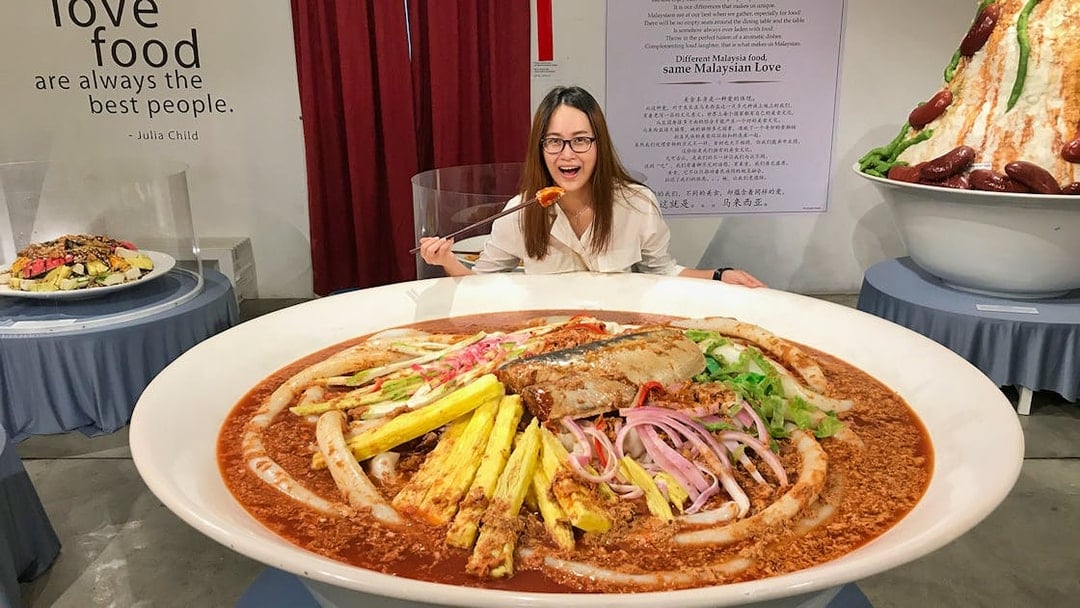 Giant bowl of Malaysian laksa at Wonderfood Museum, Penang, with a visitor posing.