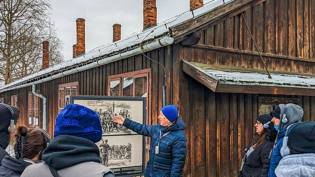 Guide explaining historical photo at Auschwitz Birkenau to tour group.