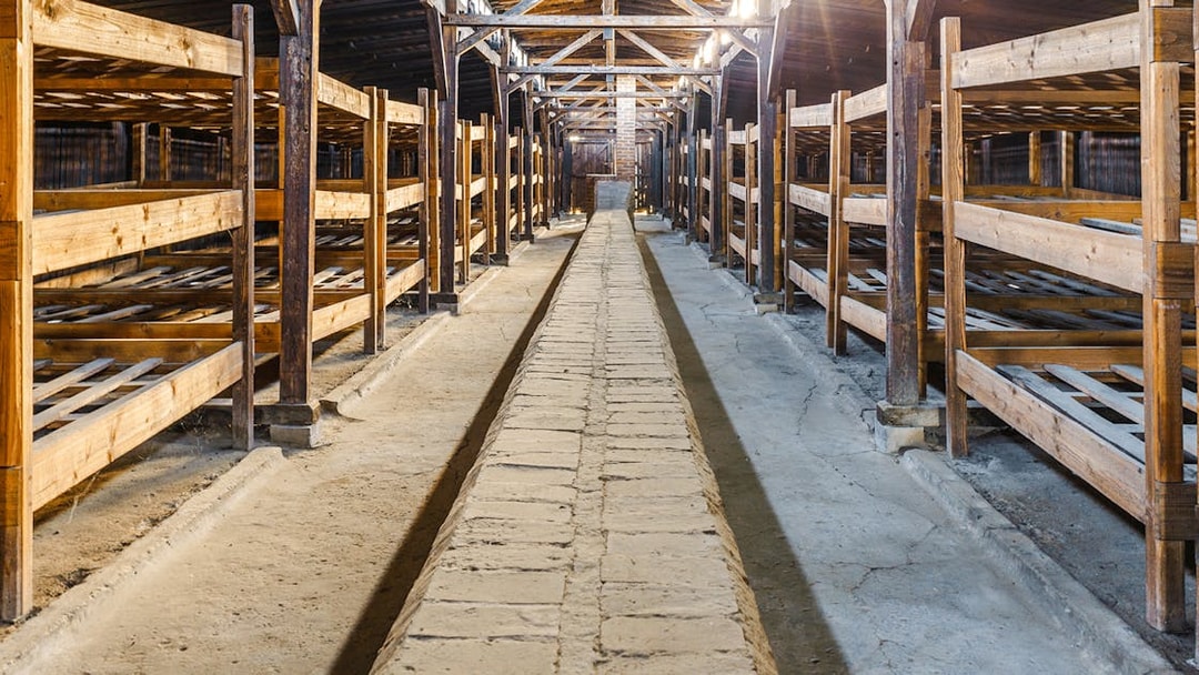 Interior of Auschwitz Birkenau barracks with wooden bunks and central walkway.