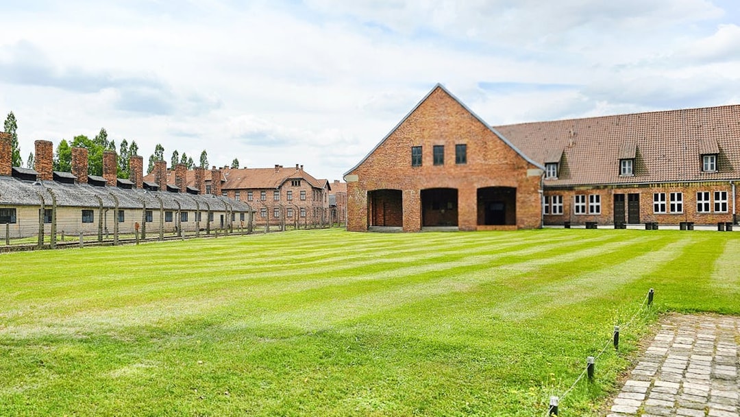 Auschwitz Birkenau barracks and main building with green lawn in foreground.