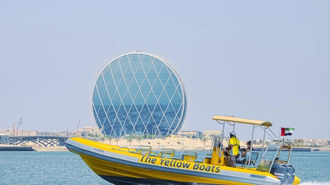 Yellow speedboat touring Yas Island with Aldar HQ building in the background.