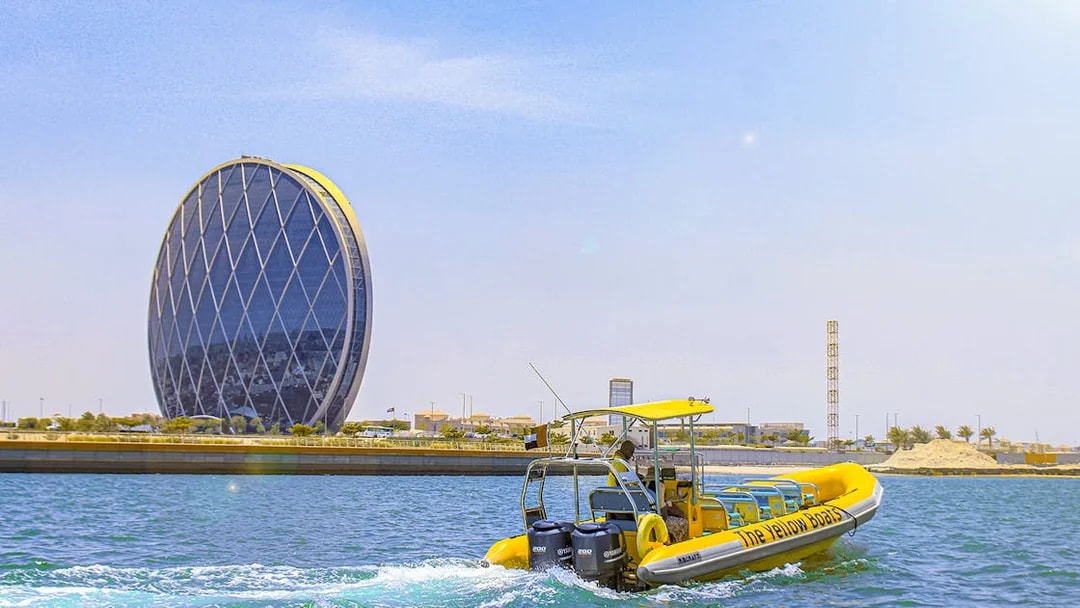 Yellow speedboat touring Yas Island with Aldar HQ building in the background.
