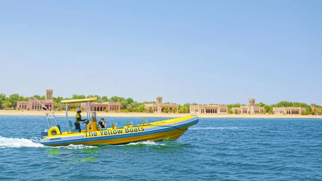 Yellow speedboat touring Yas Island with historic buildings in the background.