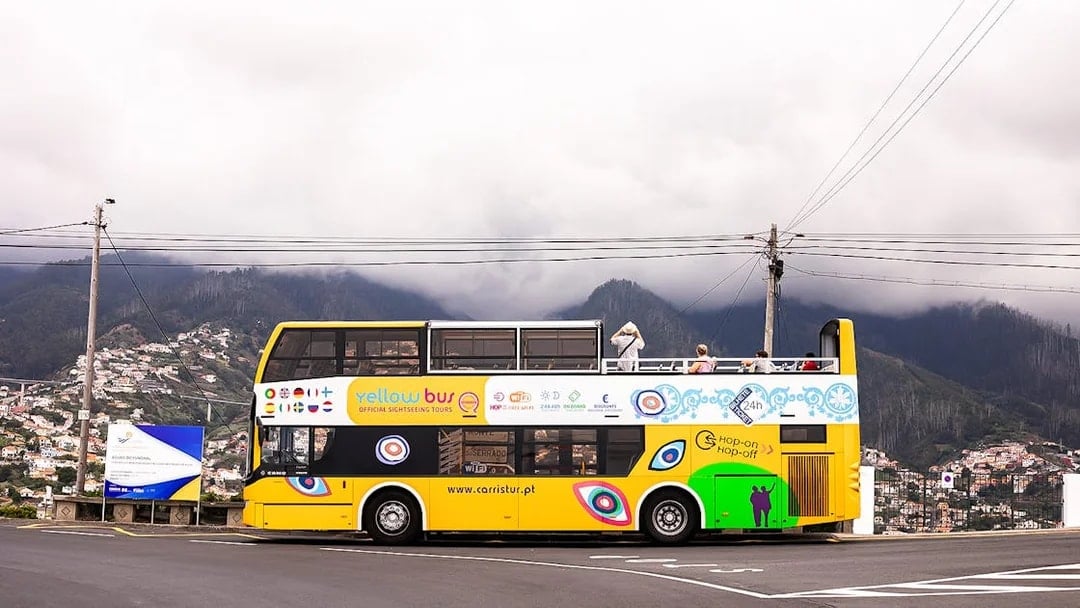 Open-top yellow tour bus on Madeira's scenic route with mountains in the background.