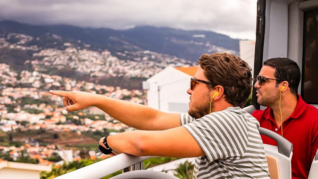 Tourists on Madeira hop-on hop-off bus enjoying city view.