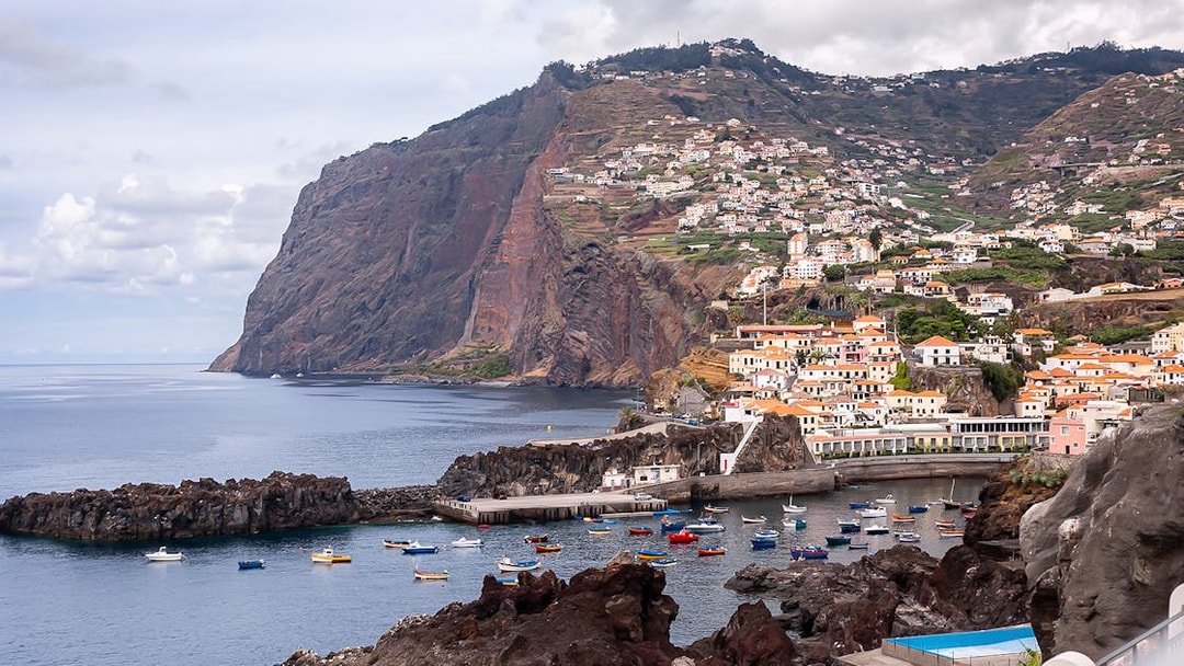 Coastal view of Madeira with colorful boats and hillside village on the 3-in-1 Hop-On Hop-Off Tour.