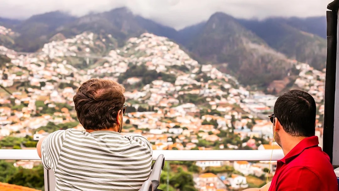 Two people enjoying a panoramic view of Madeira's mountains and cityscape on a hop-on hop-off tour.