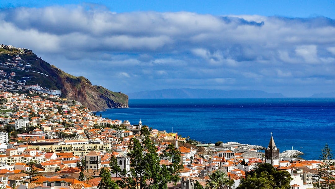 Funchal coastline view with red-roofed buildings and ocean, Madeira, Portugal.