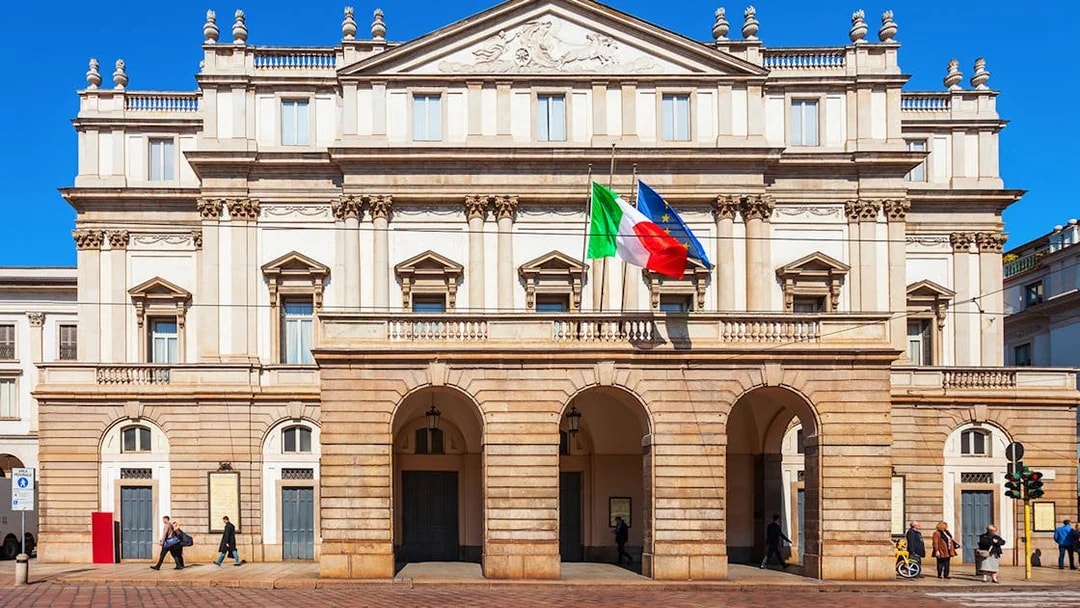 La Scala opera house facade in Milan with Italian and EU flags.