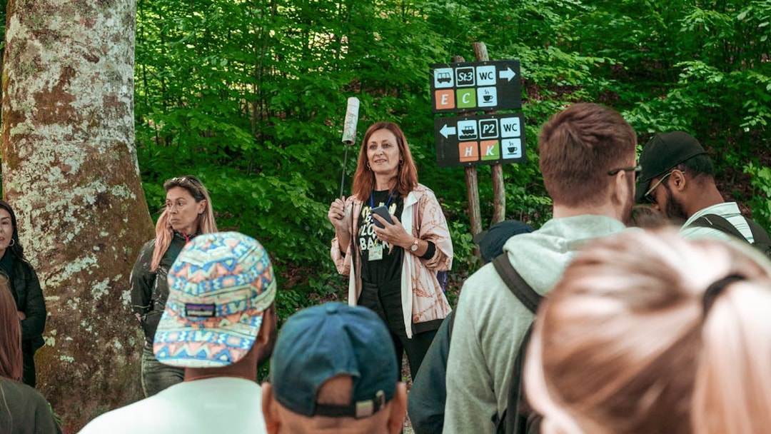 Group listening to a guide in a forested area with directional signs.