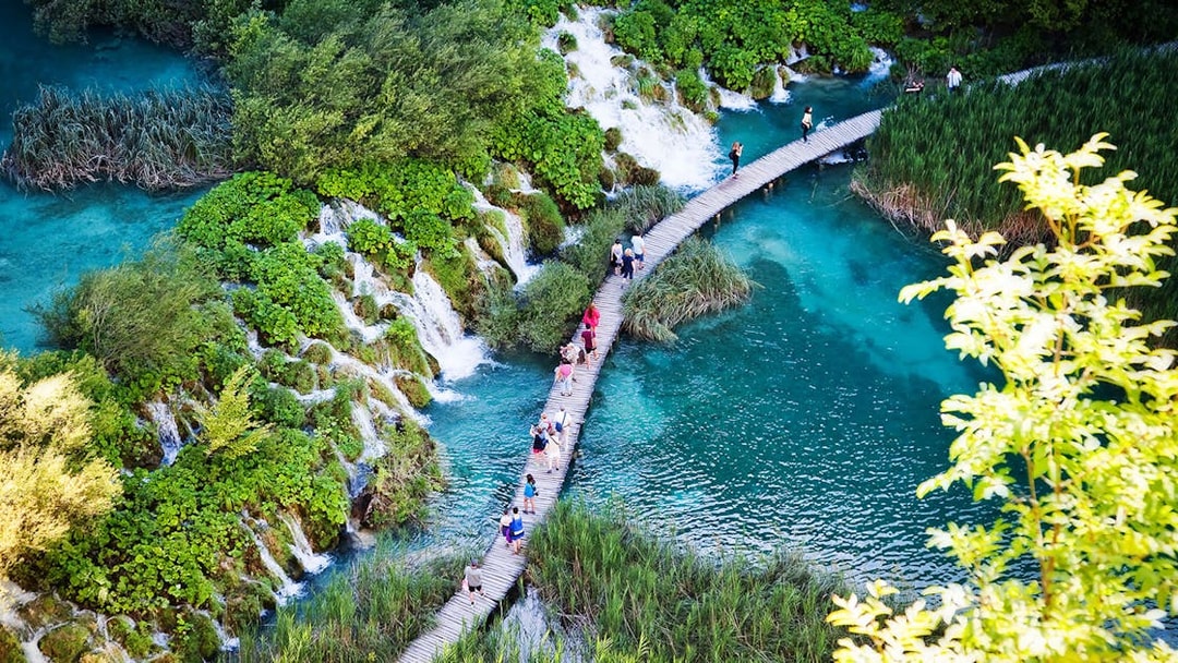 Visitors walking on a wooden path over turquoise lakes and waterfalls at Plitvice Lakes National Park.