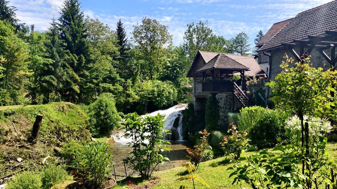 Waterfall and rustic house in lush greenery at Rastoke Village, Croatia.
