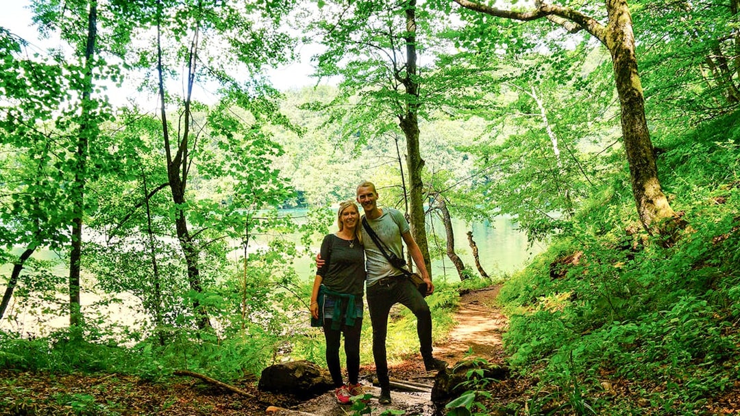 Guests walking on a forest trail by a lake in Plitvice Lakes National Park.