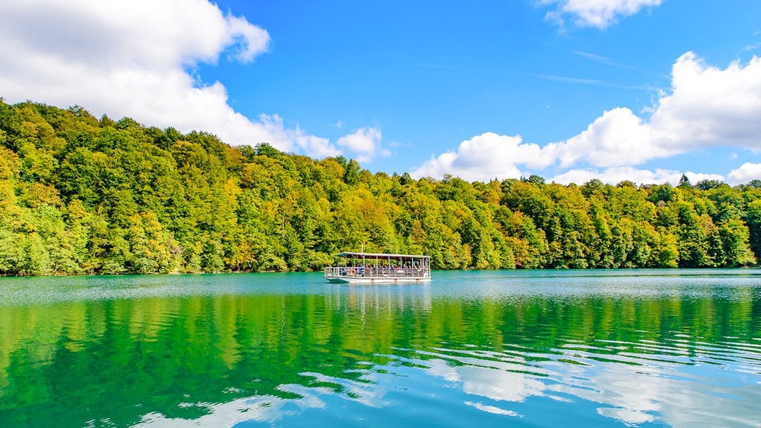 Boat on turquoise lake at Plitvice Lakes National Park with forest backdrop.