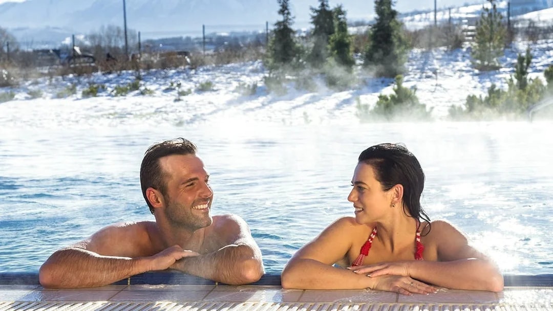 Tourists relaxing in a thermal spa with snowy Zakopane mountains in the background.