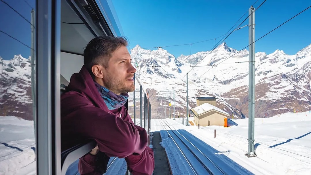 Man enjoying scenic view from train to Gornergrat, snowy mountains in background, Zermatt.