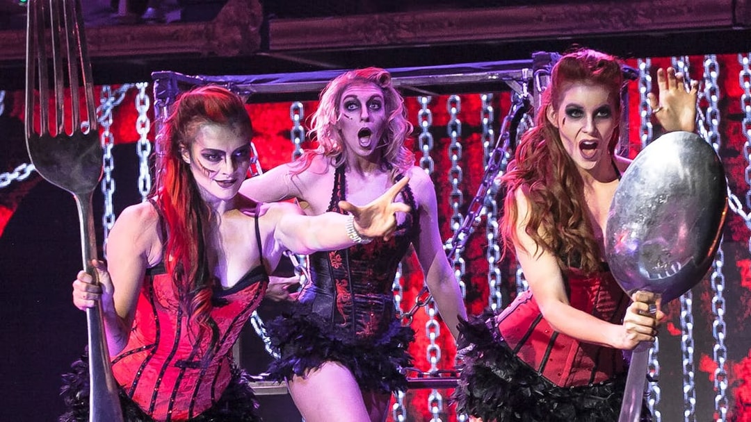 Performers in zombie-themed burlesque show with oversized fork and spoon props.
