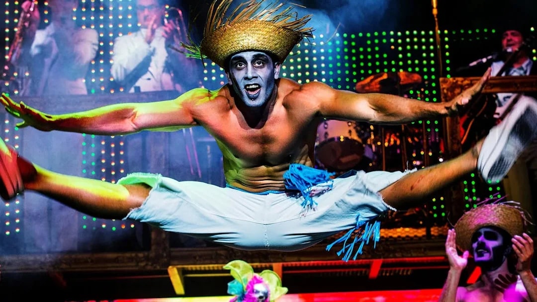 Performer in mid-air split during Zombie Burlesque show with vibrant stage lights.