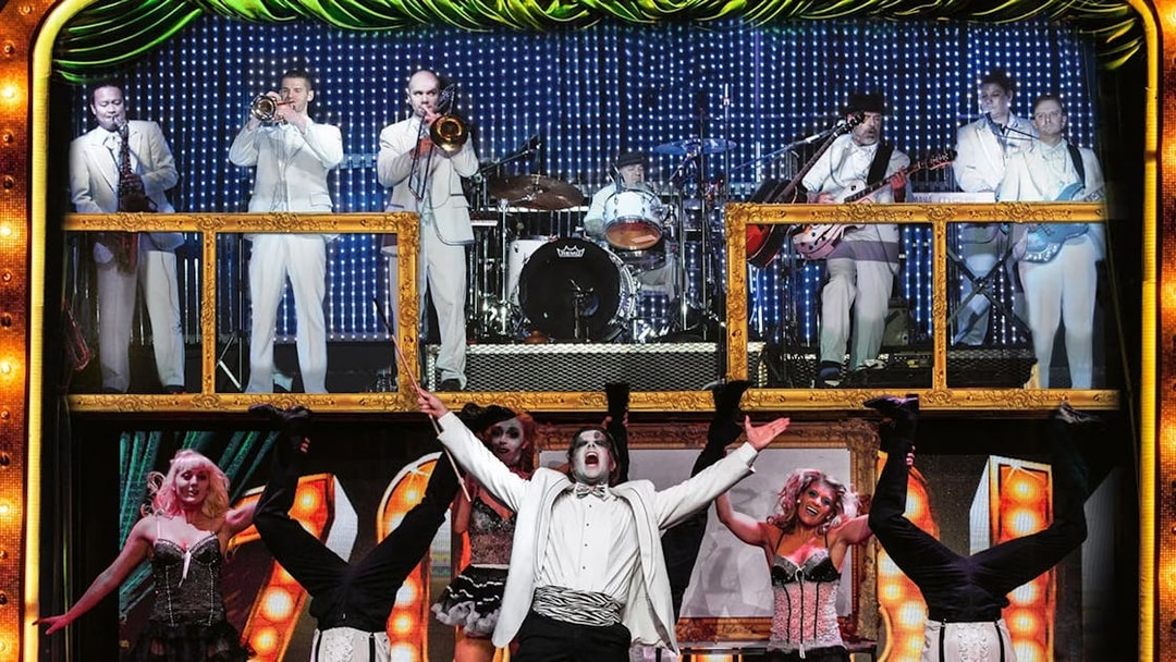 Performers in zombie-themed burlesque show with live band in background.