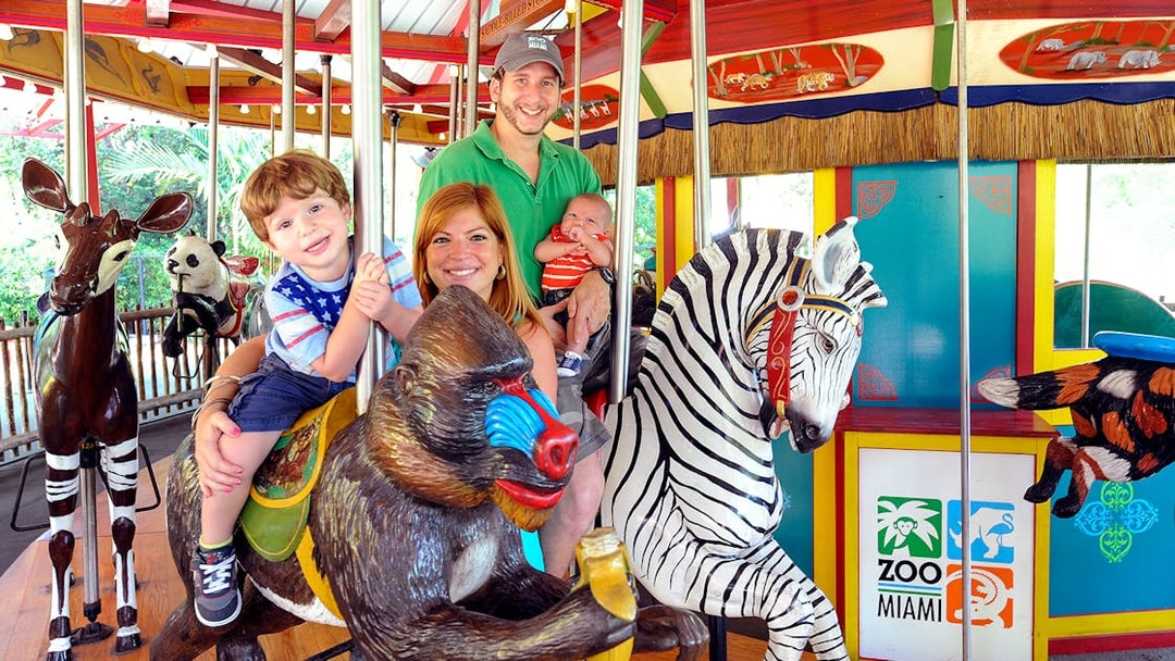 Family enjoying carousel ride at Zoo Miami with animal figures.