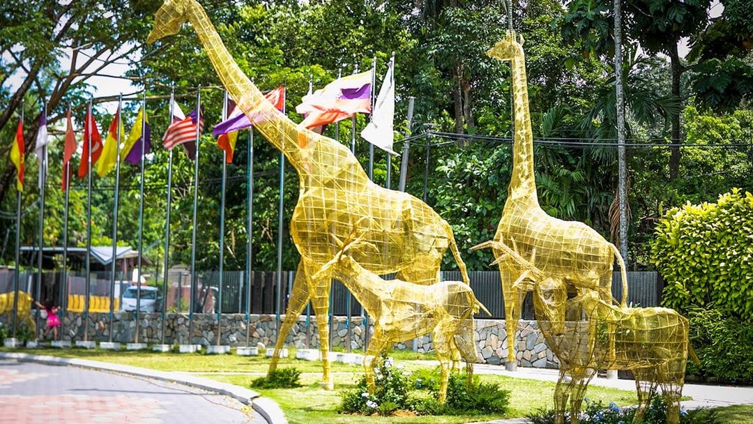 Golden giraffe sculptures at Zoo Negara entrance, Kuala Lumpur, with flags in the background.